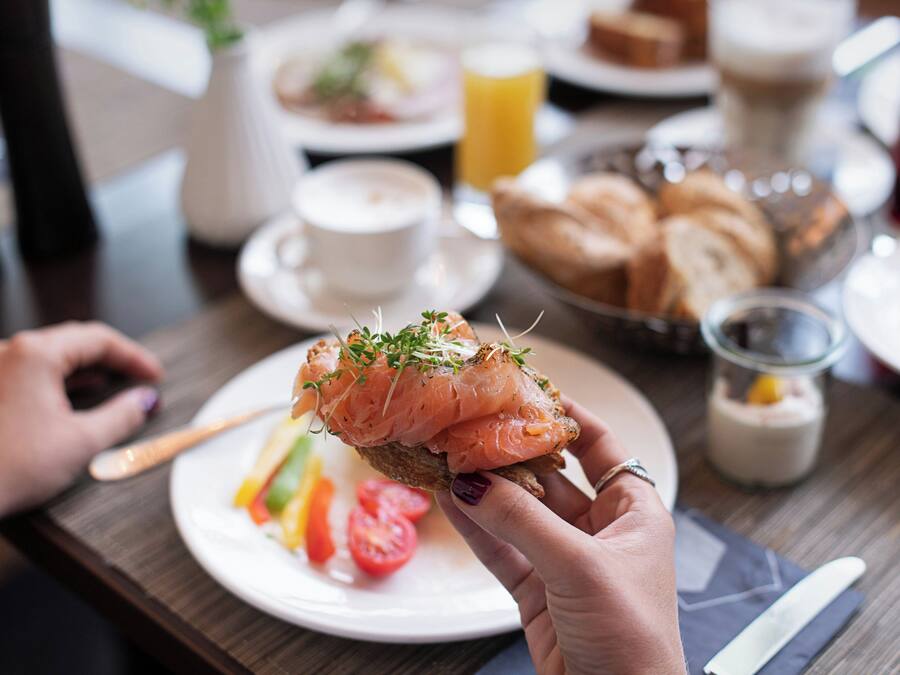 Un repas composé de toasts garnis de saumon fumé, une tasse de café et un verre de jus d’orange, le tout sur une table.