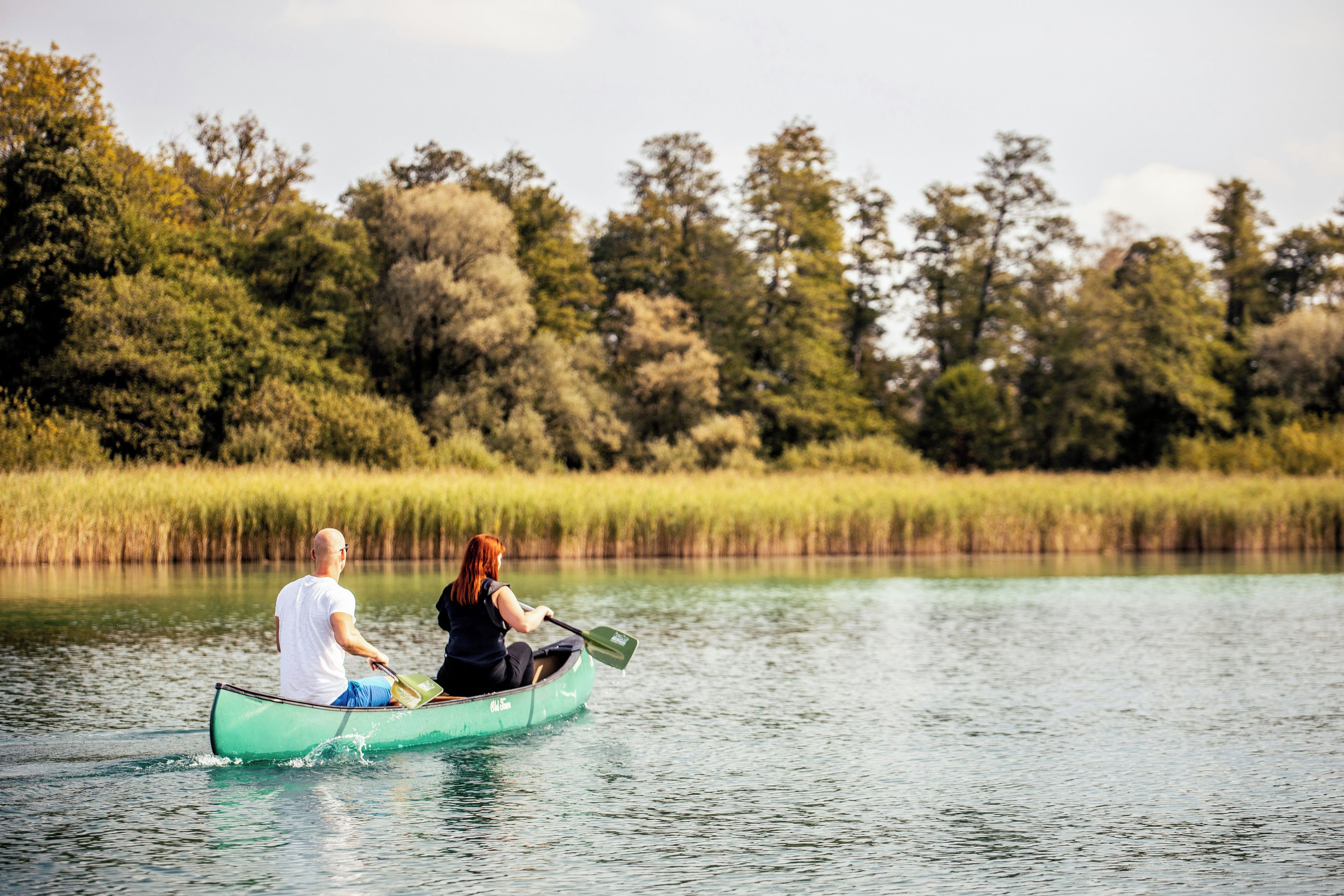 Dues persones en una canoa sobre un cos d'aigua tranquil·la, amb una riba boscosa.