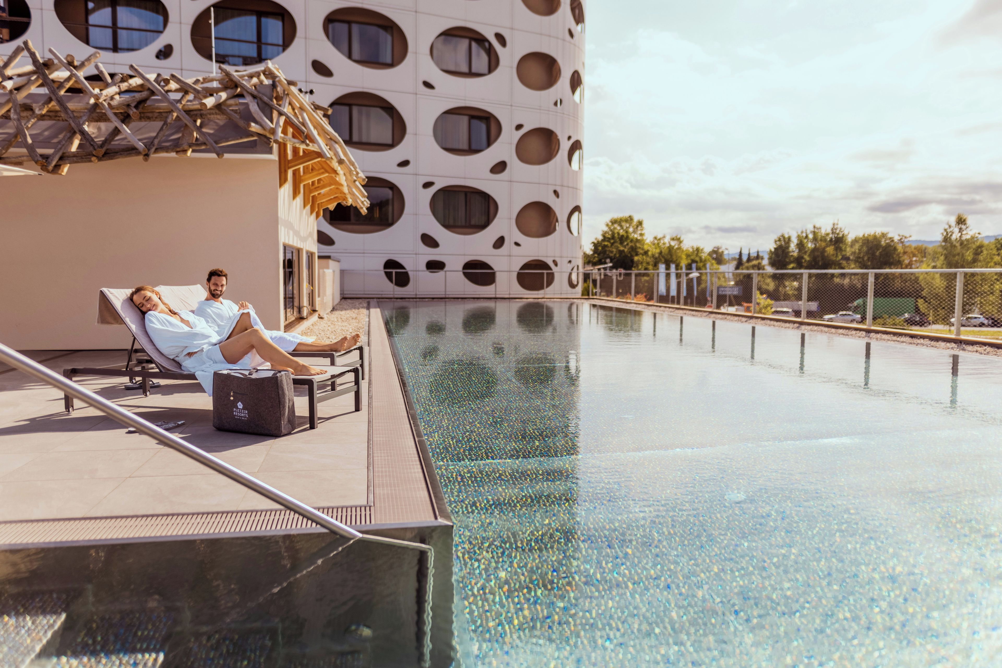 Ein Poolbereich mit zwei Liegestühlen, einer Holz-Pergola und einem modernen Gebäude mit Rundfenstern.