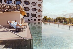 A poolside area with two lounge chairs, a wooden pergola, and a modern building with circular windows. - Seepark Wörthersee Resort (Klagenfurt am Woerthersee)