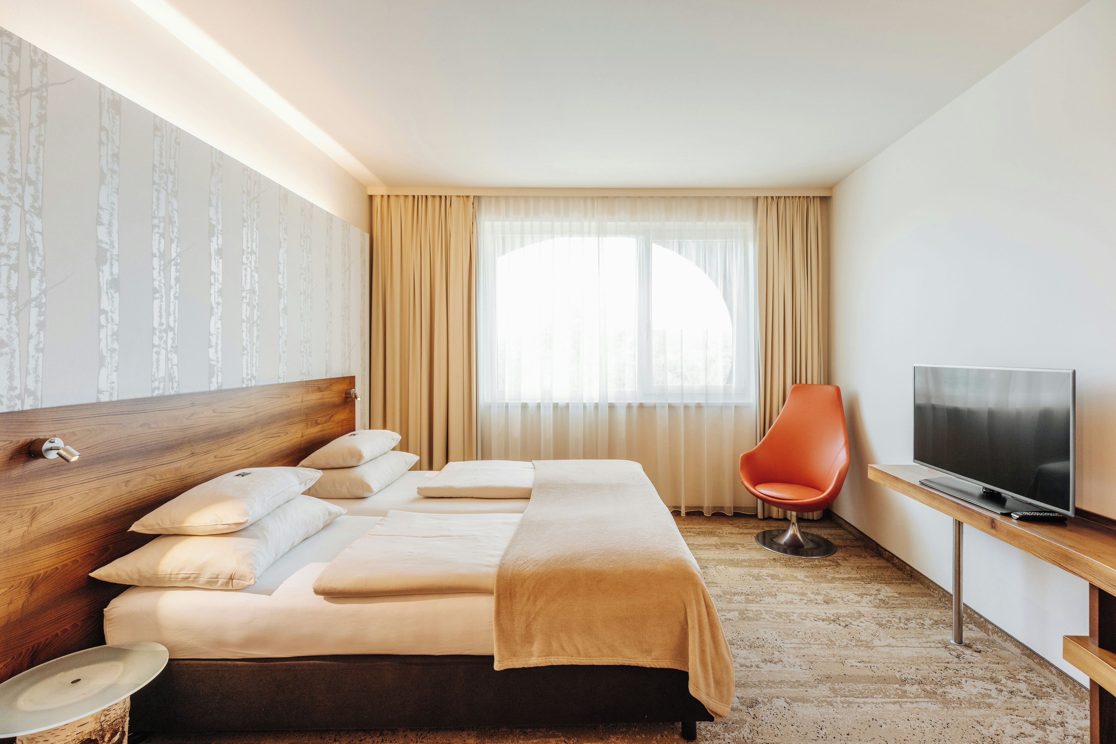 Une chambre d’hôtel avec un lit, une télévision, une chaise et une fenêtre avec des rideaux.