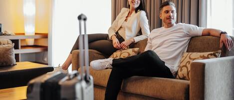 A couple sitting on a sofa with a suitcase in the foreground, suggesting a hotel setting.