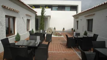 Un espacio de patio al aire libre con mobiliario de mimbre negro, plantas en macetas y piso de ladrillo.