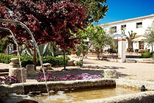A courtyard with a fountain, stone structures, and a building with windows and doors.