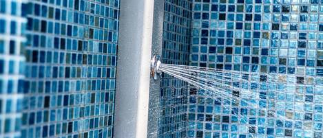 Een douche met blauwe mozaïektegels en stromend water uit een chroomkraan.