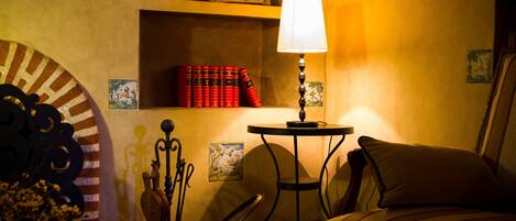 Una habitación acogedora con una lámpara, una silla, una mesa y una estantería llena de libros.