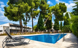 A swimming pool with lounge chairs, surrounded by trees and a building with a modern design.