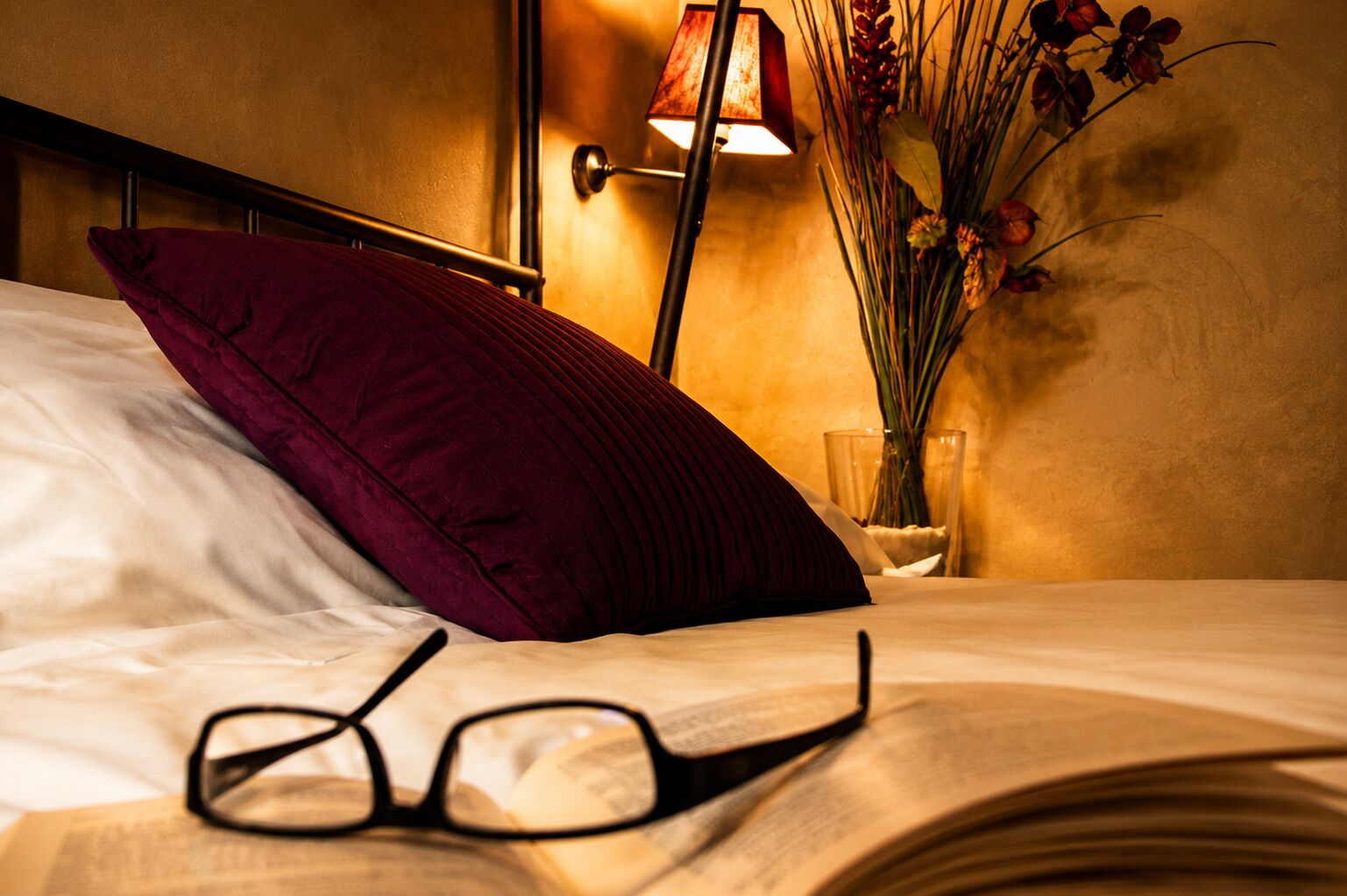 Una cama con un almohadón rojo, un par de gafas y una lámpara de noche.