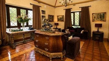 A room with a wooden floor, a large wooden dresser, a sofa, a table with a vase of flowers, and a chandelier.