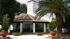 A building with a tiled roof, a white tower, and a covered patio area with potted plants. - Hotel & Spa La Salve (Torrijos)