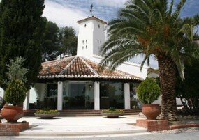 A building with a tiled roof, a white tower, and a covered patio area with potted plants.