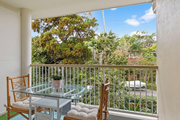 A balcony with a glass table, white cushioned chairs, and a potted plant.