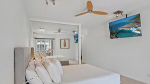 A bedroom with a bed, a ceiling fan, a TV, and a view of the ocean. - Serenity Apartments Noosa (Noosa Heads)
