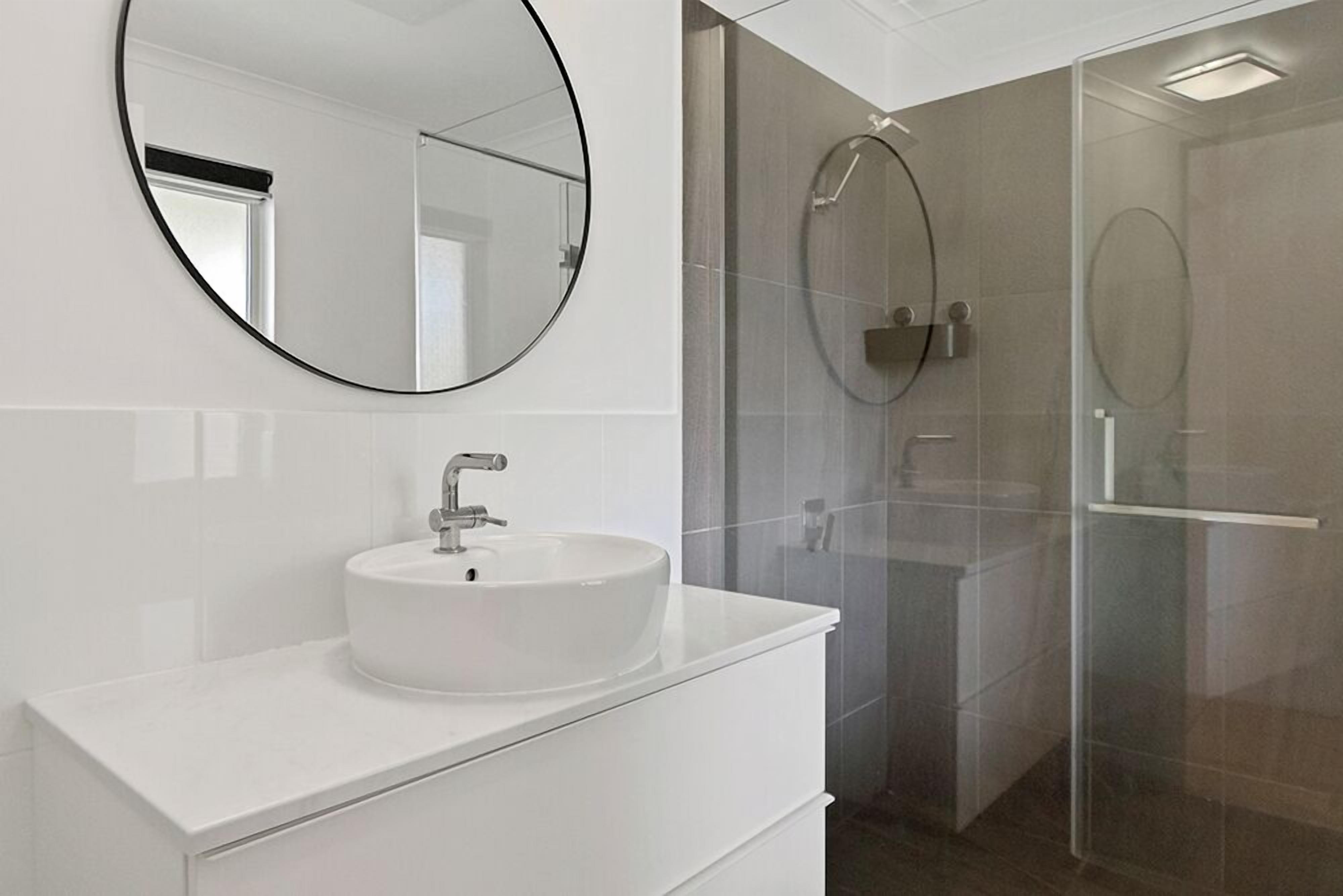 A modern bathroom with a round mirror, a white sink, and a glass shower enclosure.