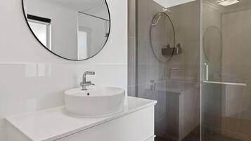 A modern bathroom with a round mirror, a white sink, and a glass shower enclosure.