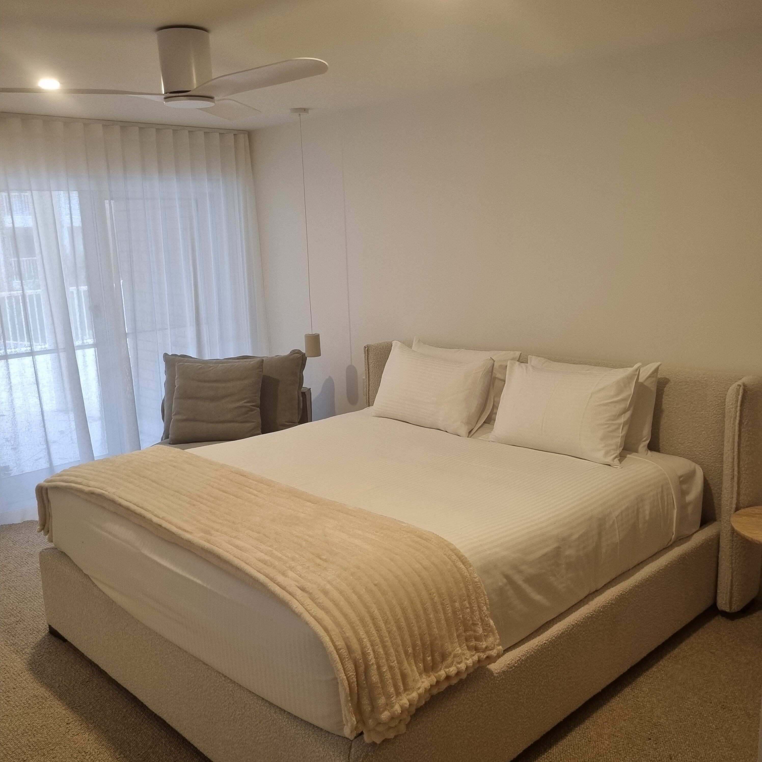 A bedroom with a large bed, a ceiling fan, and a window with sheer curtains.