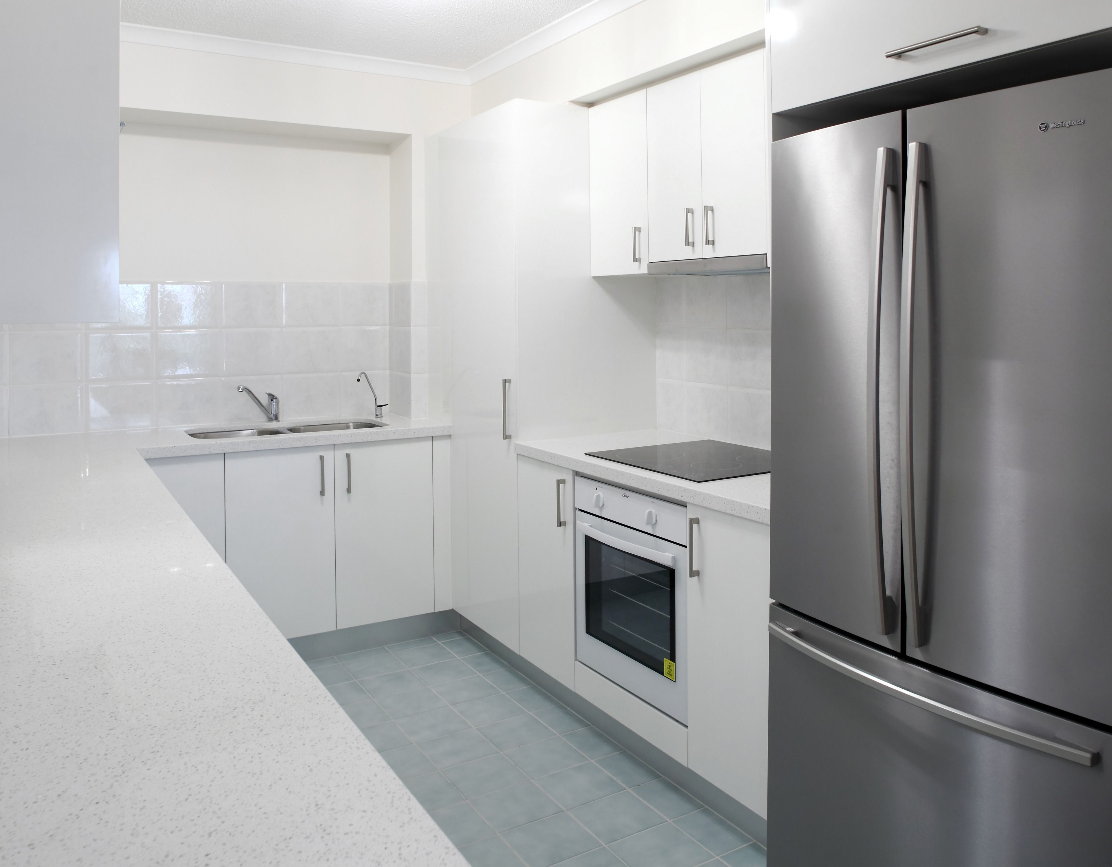 A modern kitchen with white cabinets, a stainless steel refrigerator, a built-in oven, and a sink.