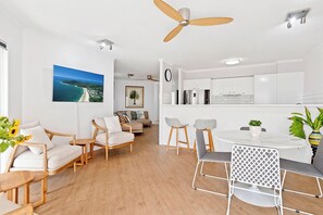 A modern living room with a sofa, chairs, a dining table, and a ceiling fan. - Serenity Apartments Noosa (Noosa Heads)