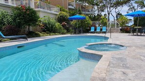 A swimming pool with a hot tub, surrounded by lounge chairs and umbrellas, set against a backdrop of a residential building with balconies. - Serenity Apartments Noosa (Noosa Heads)