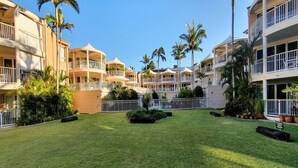A courtyard with a well-maintained lawn, palm trees, and a gated entrance. - Serenity Apartments Noosa (Noosa Heads)