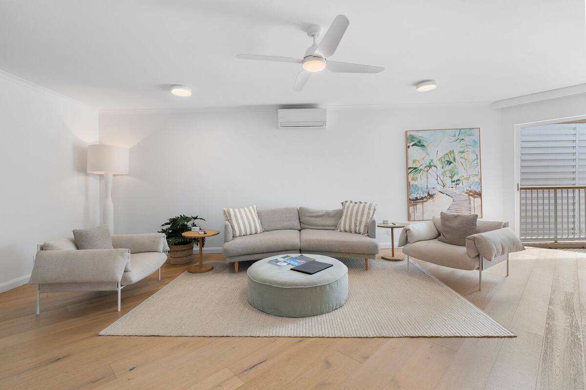 Ein modernes Wohnzimmer mit grauem Sofa, Hocker und Deckenventilator.