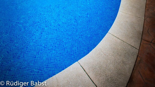 A swimming pool with clear blue water, surrounded by lounge chairs and palm trees, with buildings in the background. - Parque Tropical (Vera)