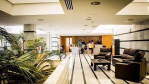 A hotel lobby with a reception desk, seating area, and decorative plants. - Parque Tropical (Vera)