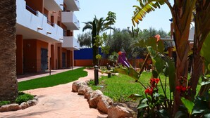 A courtyard with a stone pathway, palm trees, and a playground. - Parque Tropical (Vera)