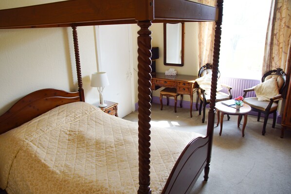 A four-poster bed with a quilt, a wooden desk with a chair, a small table with a vase, and a mirror on the wall. - Abbey Grange Hotel (Llangollen)