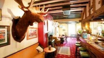 Un restaurante con un ciervo colgado en la pared, vigas de madera en el techo y un suelo cubierto de alfombra roja.