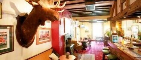 Un restaurant dont le mur est orné d’une tête d’élan empaillée, dont le plafond est décoré de poutres en bois et dont le sol est recouvert d’un tapis rouge.