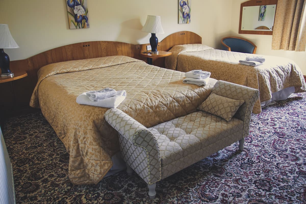 A hotel room with two beds, a sofa, a lamp, and a chair.