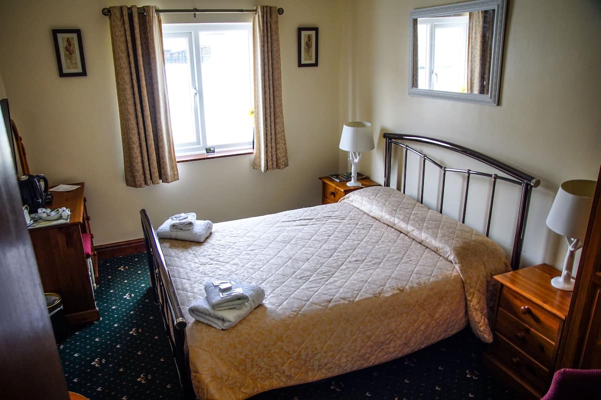 A neatly made bed with a quilt, a bedside lamp, a wooden nightstand, and a window with curtains.