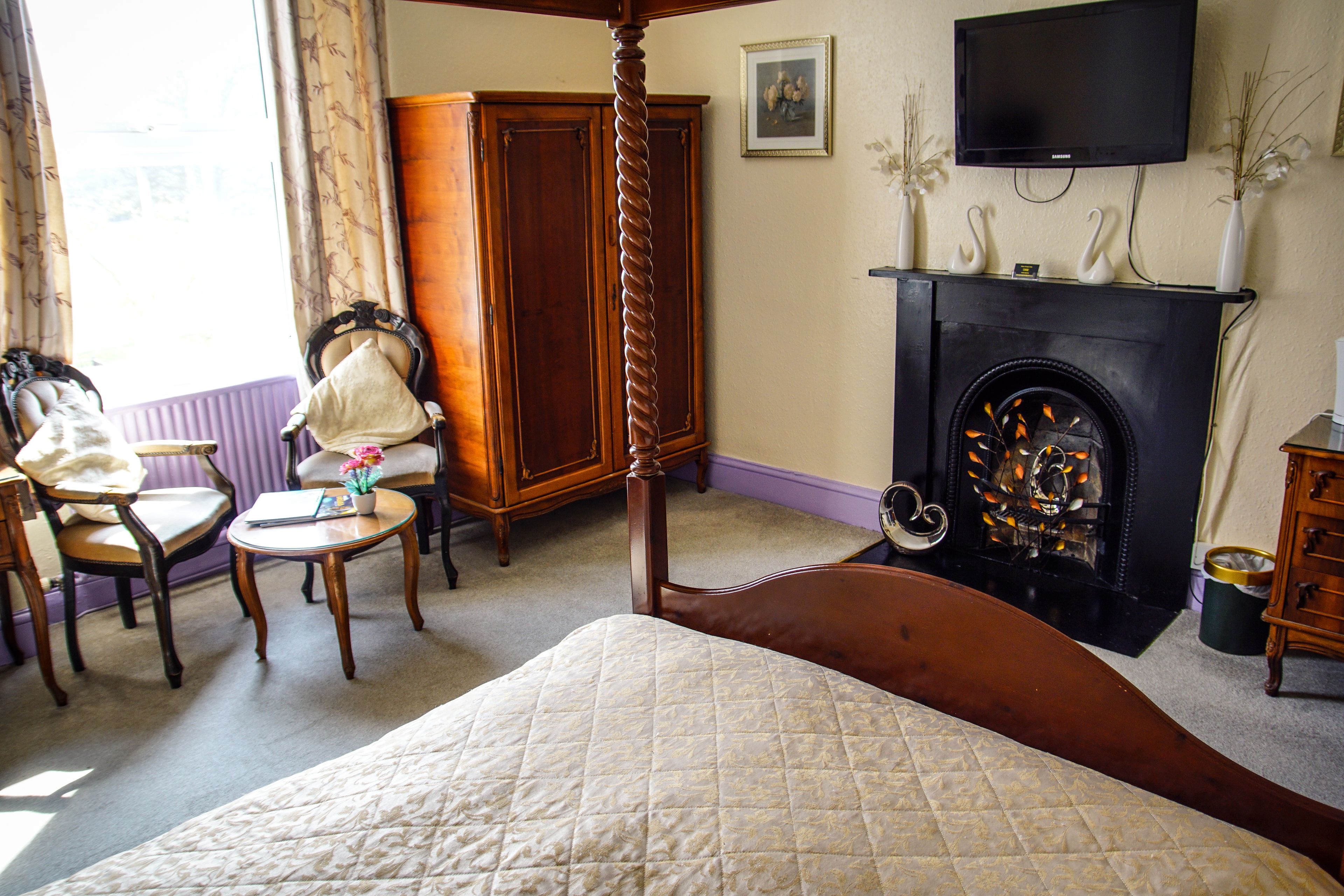 Un dormitorio con cama con dosel, chimenea, televisor montado encima y un amplio armario.