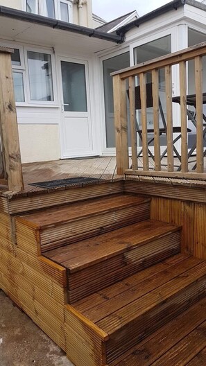 A wooden deck with steps leading to a raised platform, surrounded by a wooden railing. - The Alexander (Swansea)