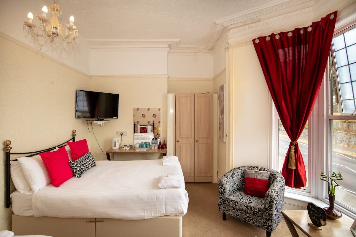 Quarto de hotel com cama, televisão, escrivaninha, cadeira e janela com cortinas.