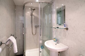 A modern bathroom with a glass-enclosed shower, a white sink, and a marble wall. - The Alexander (Swansea)
