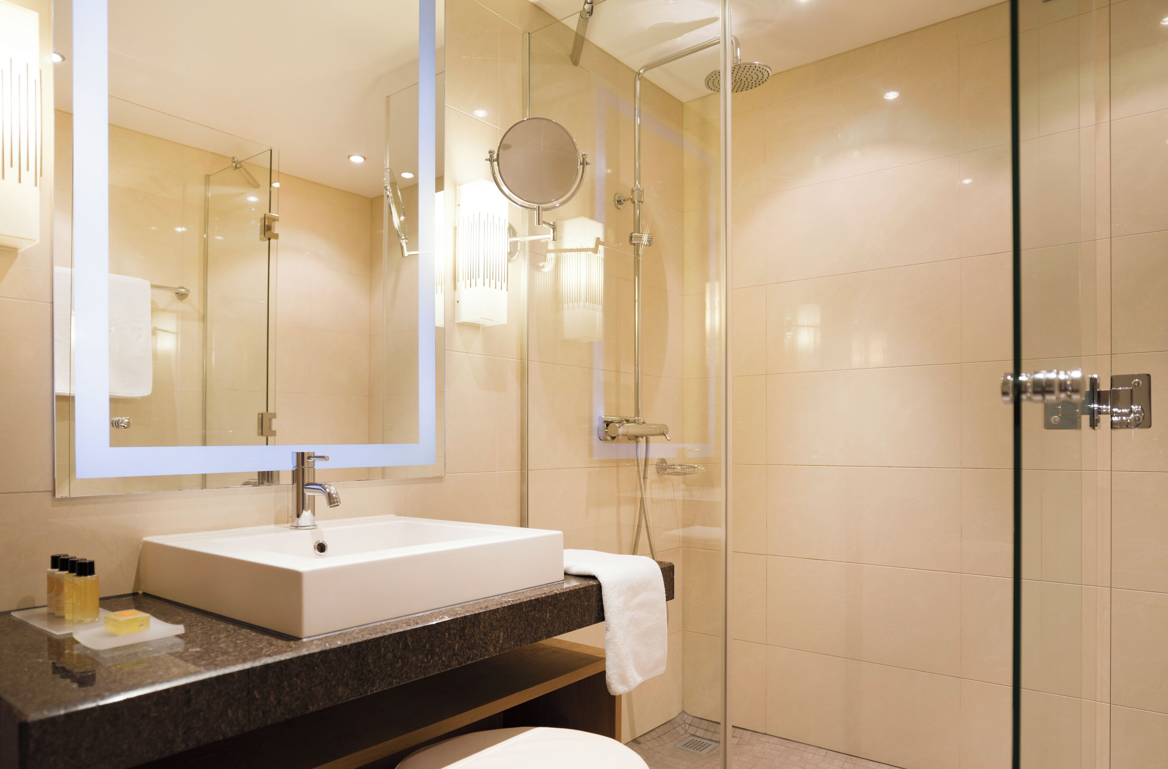 Een moderne badkamer met een douchecabine van glas, een grote spiegel en een wit wastafelmeubel.