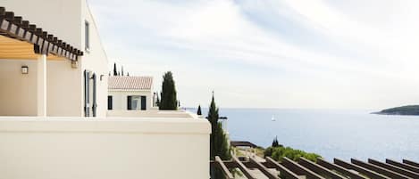 A coastal building with a terrace overlooking the sea, featuring a pergola and a view of the ocean.