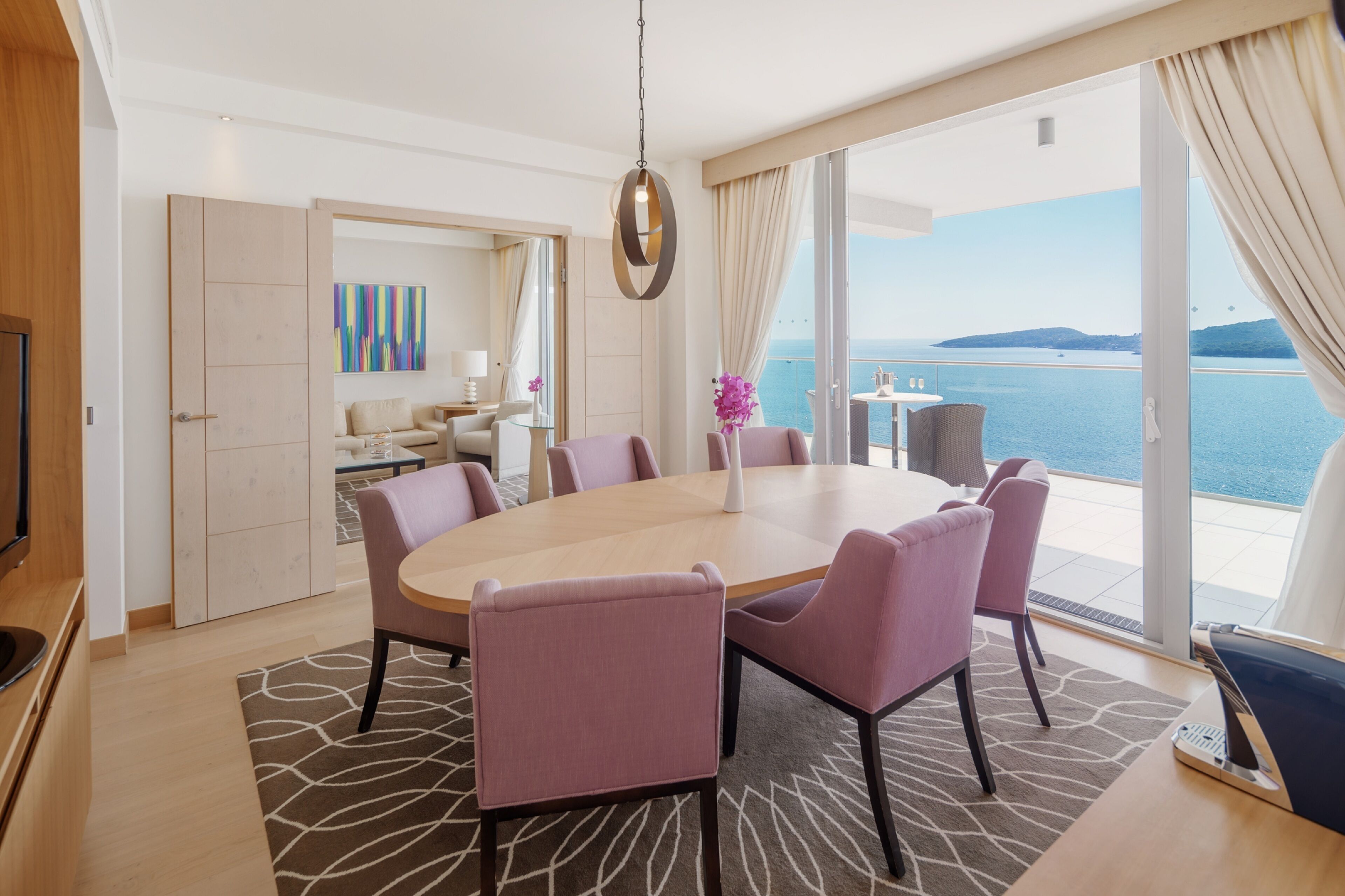 Un espace repas moderne avec une table ronde, six chaises et une vue sur la mer.