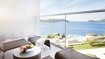 A balcony with wicker furniture, a bowl of fruit, and a view of the sea and hills.
