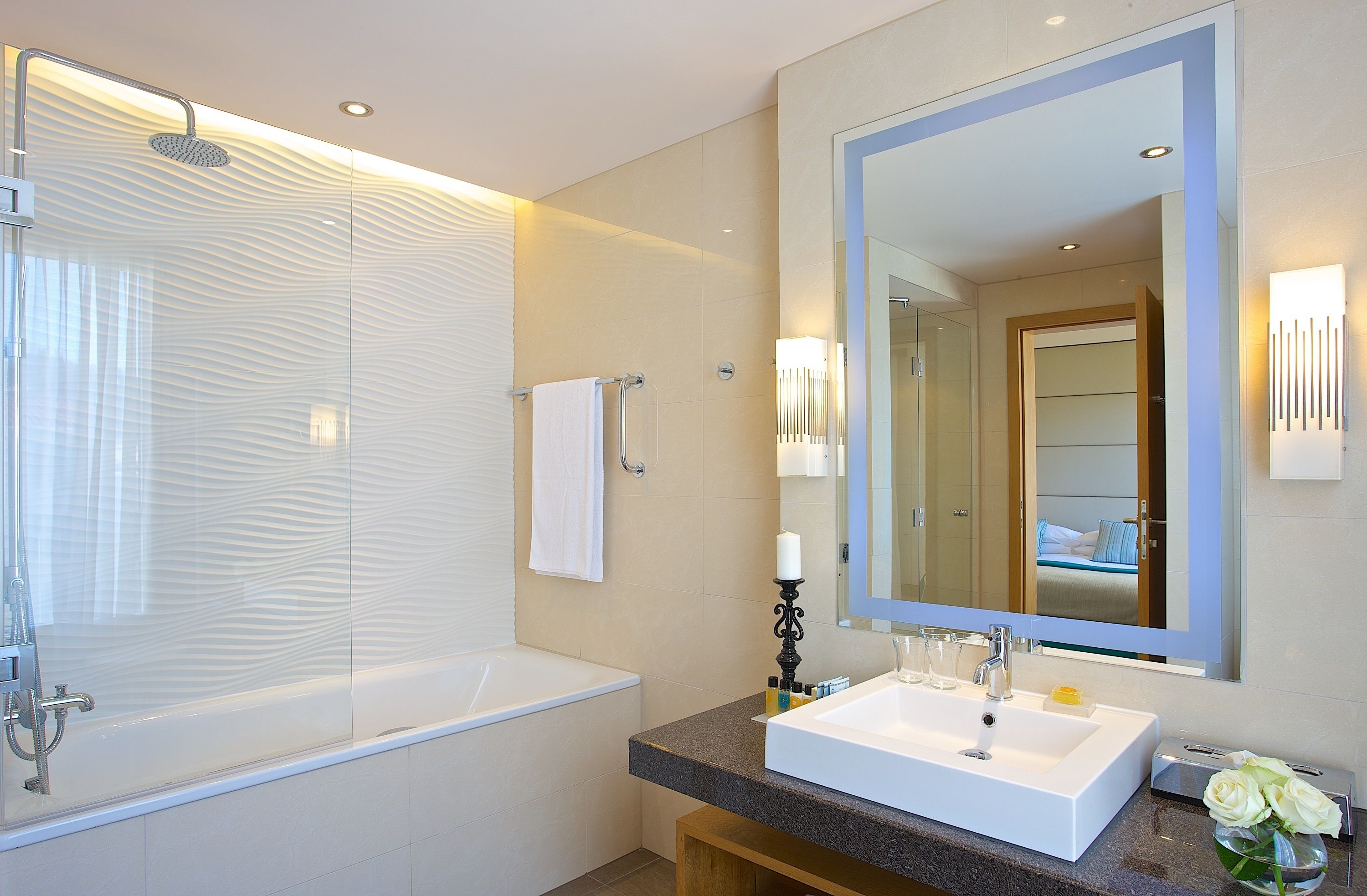 Un bagno moderno con cabina doccia in vetro, una vasca da bagno bianca, uno specchio grande e un lavabo con piano in granito.