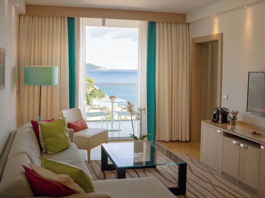 Een moderne hotelkamer met een bank, een glazen salontafel, een televisie en uitzicht op zee.