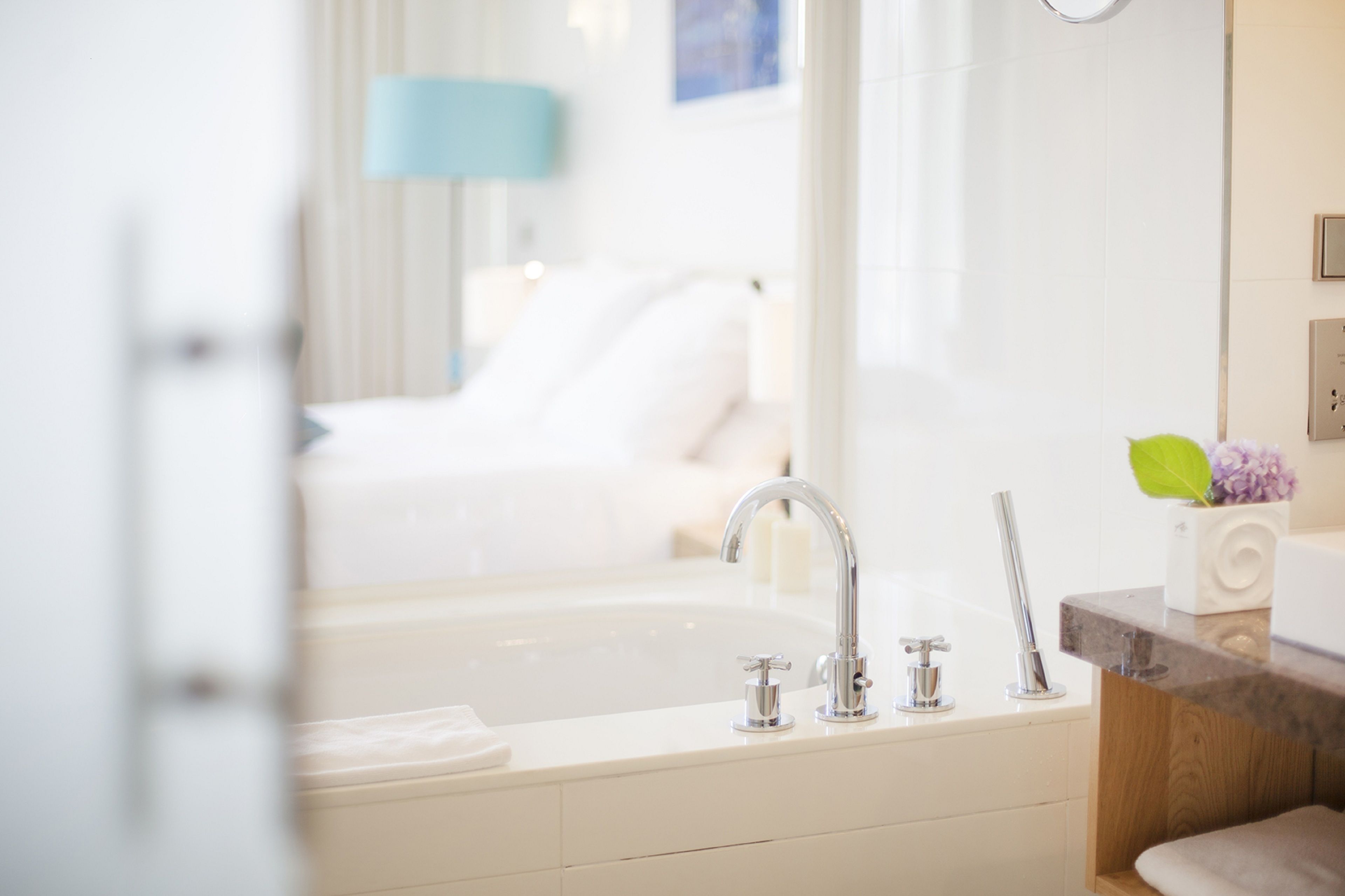 A modern bathroom with a bathtub, a sink with two faucets, and a vanity with a mirror.