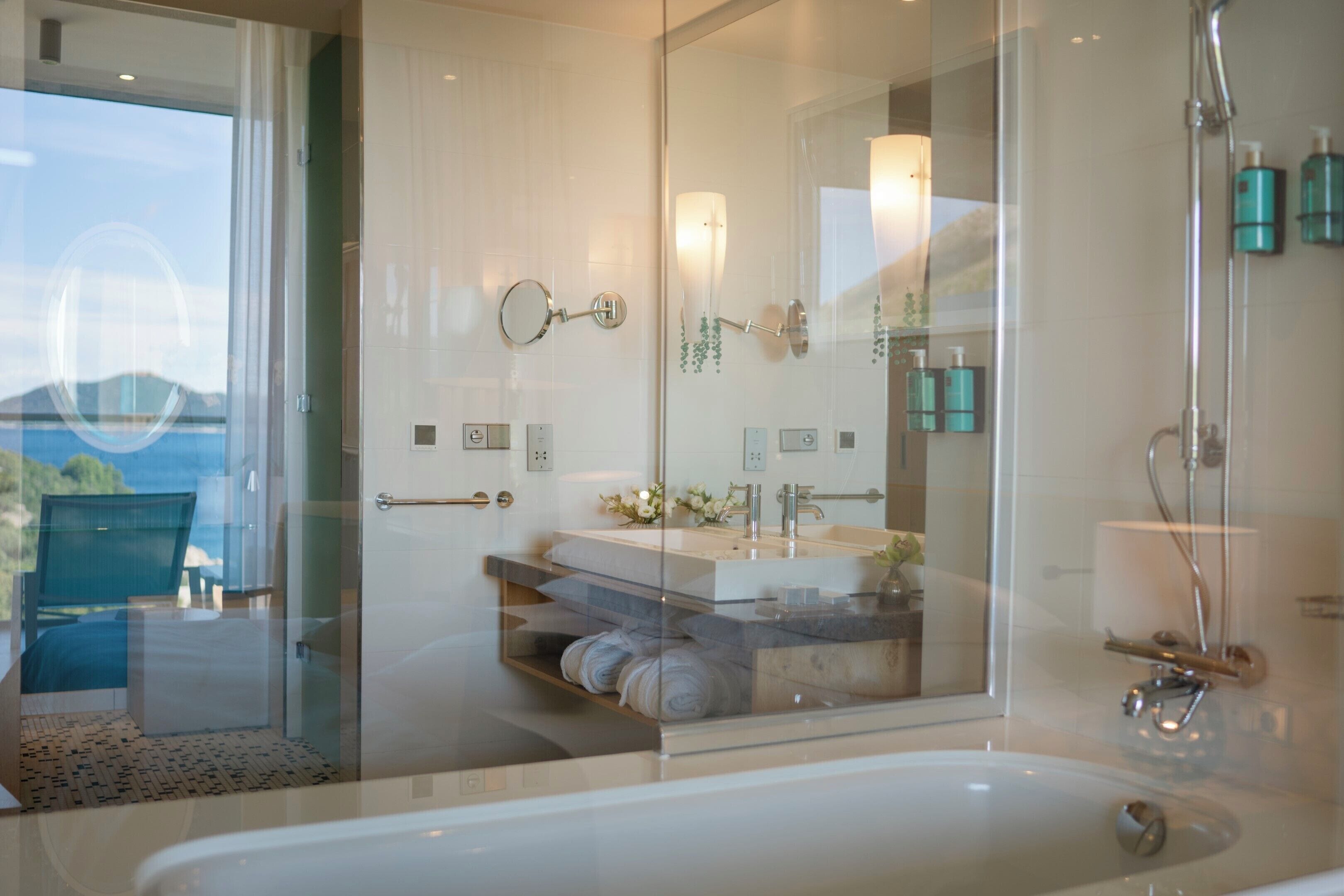 A modern bathroom with a glass shower enclosure, a bathtub, and a vanity with a mirror and towel rack.