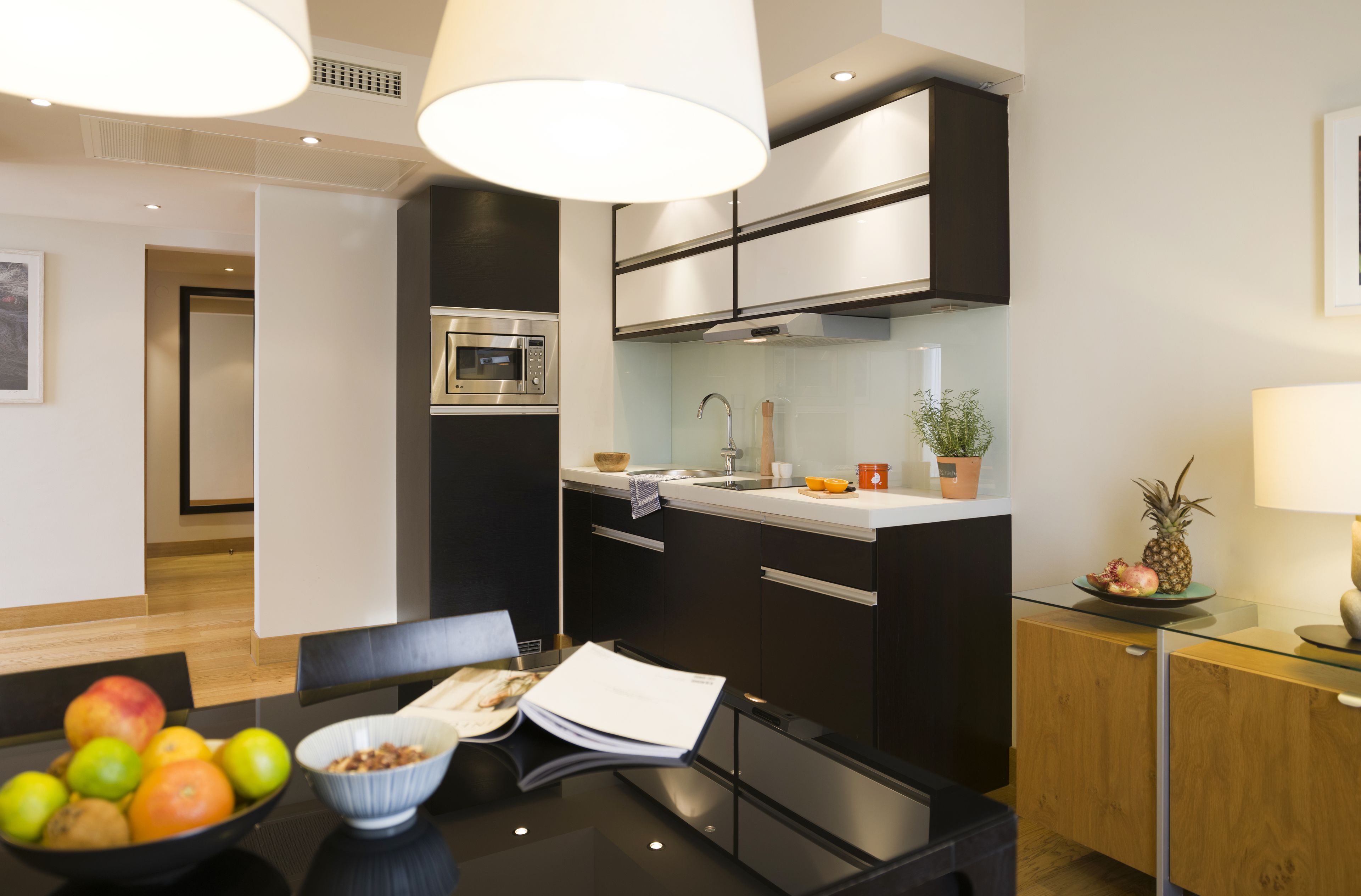 A modern kitchen with black cabinets, a microwave, and a sink. There is a bowl of fruit on the counter and a potted plant on the island.