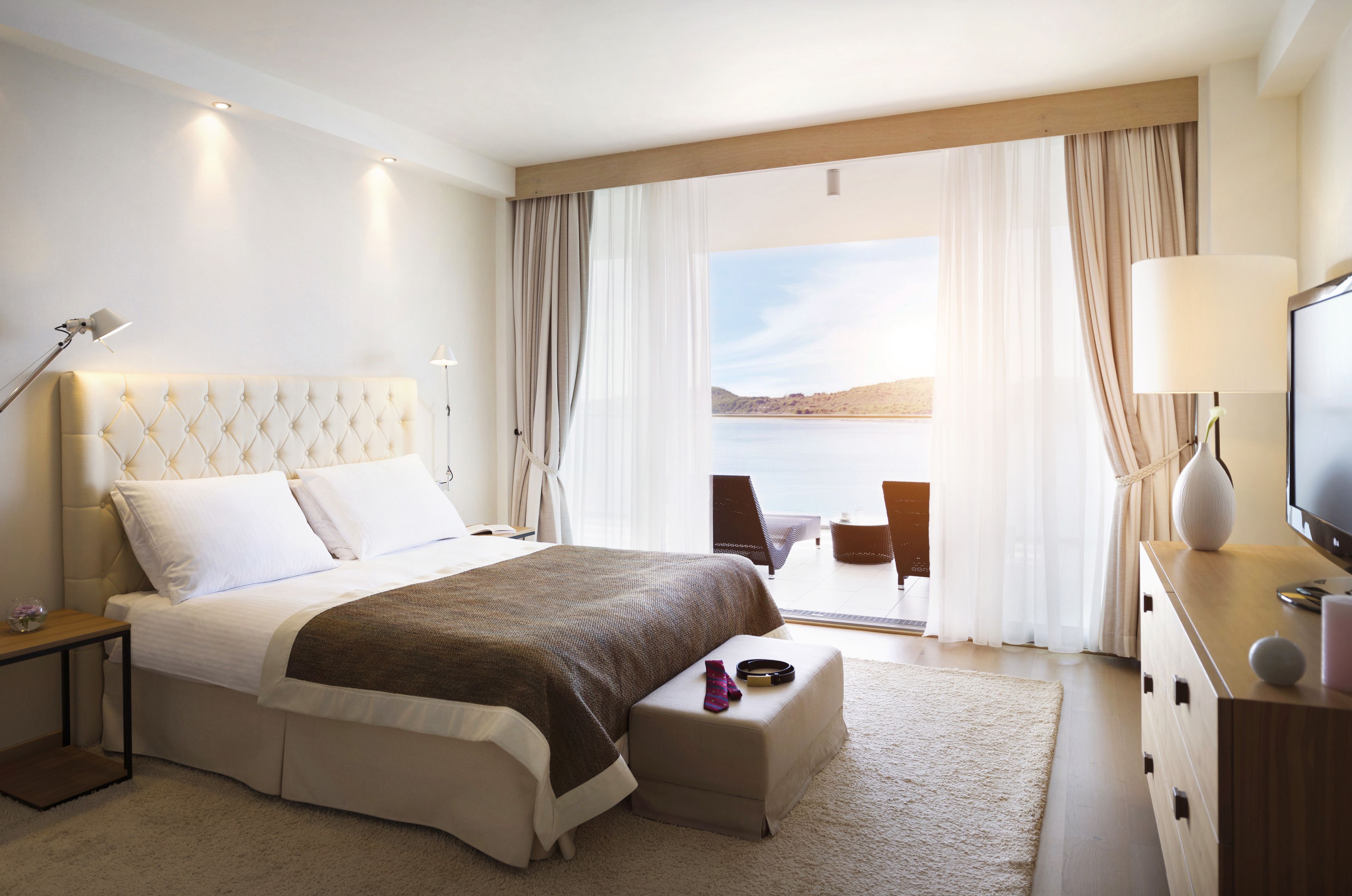 A hotel room with a large bed, a TV, a desk, and a view of the sea.