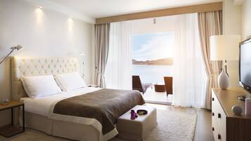 A hotel room with a large bed, a TV, a desk, and a view of the sea.