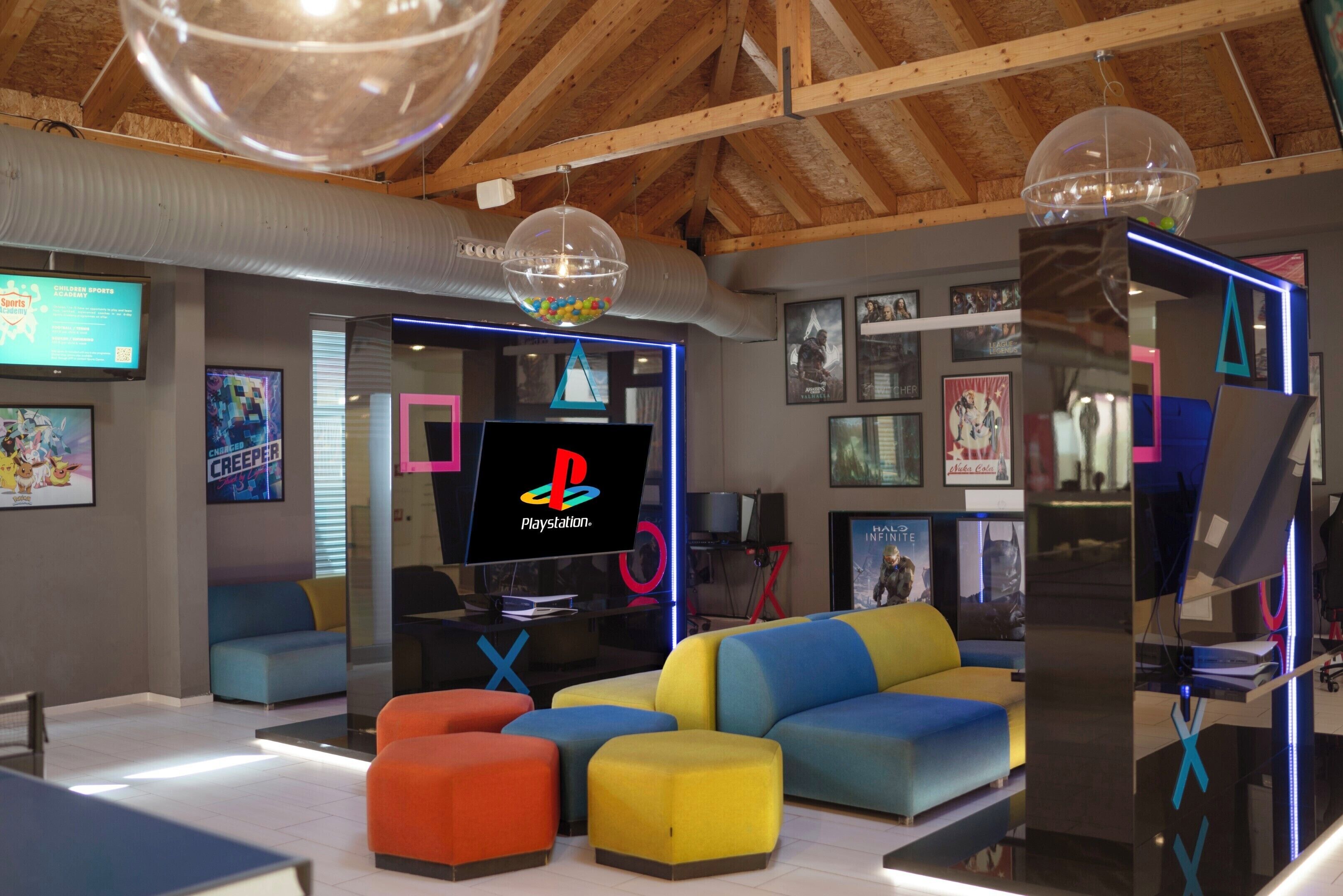 Un salón de juegos moderno con asientos coloridos, un televisor PlayStation y varios carteles.