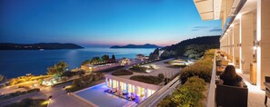 Un hotel con piscina, mobiliario exterior y vistas a un lago y colinas.